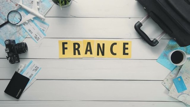 Top view time lapse hands laying on white desk word "FRANCE" decorated with travel items