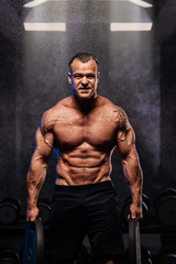 Fototapeta na wymiar Muscular bodybuilder posing with weights in gym.
