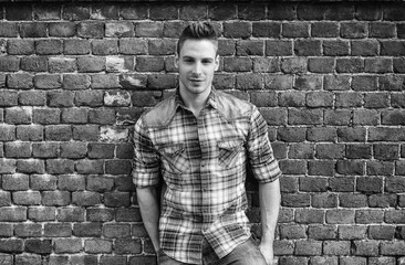 Smiling young man leaning on old brick wall, wearing blue and red shirt and jeans