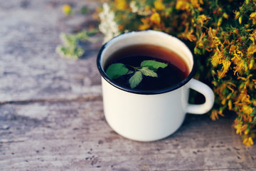 Herbal tea in an iron mug and St. John's Wort flowers on an old wooden surface of a table, soft focus