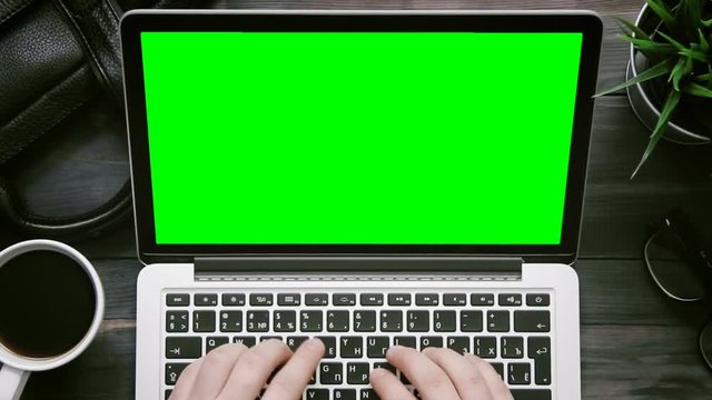 Top view male hands working on laptop computer with green screen at white desk from above