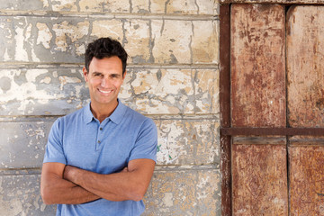 cool middle age man smiling with arms crossed against wall