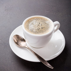 White cup of coffee on dark brown background with copy space.