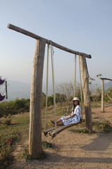Thai woman sit and play on wooden bench swings toy at posing on top of Phu Pa Po mountain or Fuji City Loei