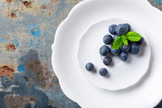 Fresh blueberries on white plate on old rusty blue background. Healthy eating and nutrition concept with copy space. Top view.