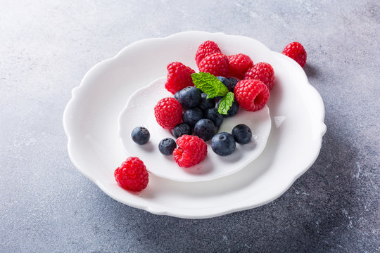Freshly picked blueberries and raspberries on white plate on gray stone background. Concept for healthy eating and nutrition with copy space.
