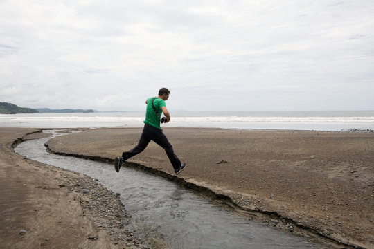 Man jumping over stream on beach