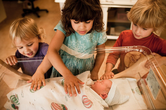 Siblings looking at newborn baby brother in hospital
