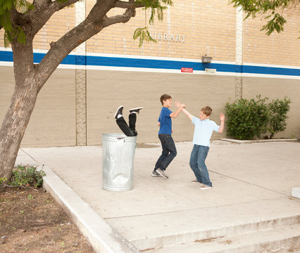 Two boys bullying another, one boy in dustbin