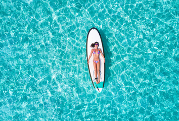 Attraktive Frau im Bikini sonnt sich auf einem Surfbrett über dem türkisen Wasser der Malediven