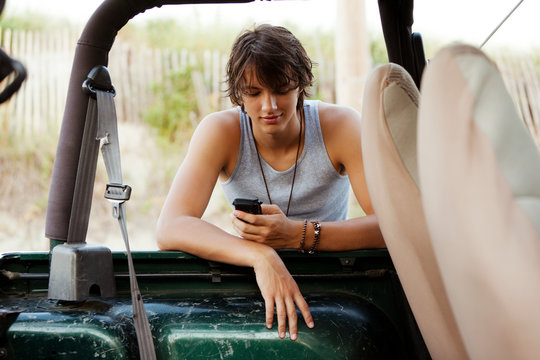 Teenager leaning against jeep checking phone