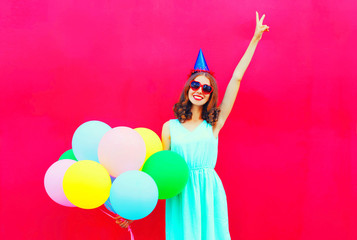 Obraz na płótnie Canvas Happy smiling woman in a birthday cap having fun over an air colorful balloons pink background