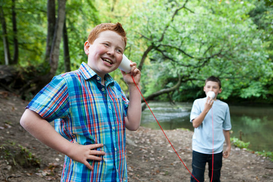 Two boys using paper cups and string to communicate in woodland