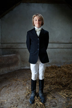 Boy standing in horse riding clothes in stable