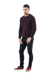 Sad young man with hands in pockets wearing sweater looking at camera. Full body length portrait...