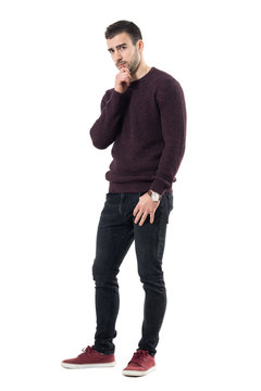 Skeptical Suspicious Man With Hands On Chin Looking At Camera Distrustful. Full Body Length Portrait Isolated Over White Studio Background.