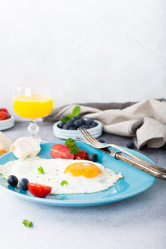 Fried egg on blue plate, tomatoes, blueberries, mint tea and orange juice. Healthy breakfast concept with copy space.