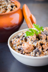 Buckwheat porridge with mushrooms and chicken in a ceramic pot on grey background. Healthy dinner. Top view. Selective focus.