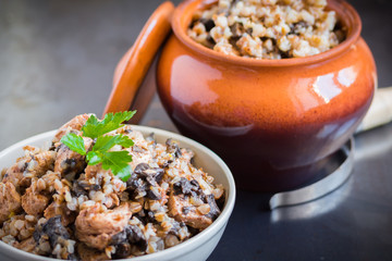 Buckwheat porridge with mushrooms and chicken in a ceramic pot on grey background. Healthy dinner. Top view. Selective focus.