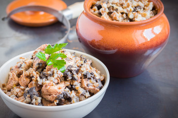 Buckwheat porridge with mushrooms and chicken in a ceramic pot on grey background. Healthy dinner. Top view. Selective focus.