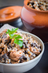 Buckwheat porridge with mushrooms and chicken in a ceramic pot on grey background. Healthy dinner. Top view. Selective focus.