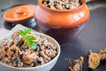 Buckwheat porridge with mushrooms and chicken in a ceramic pot on grey background. Healthy dinner. Top view. Selective focus.