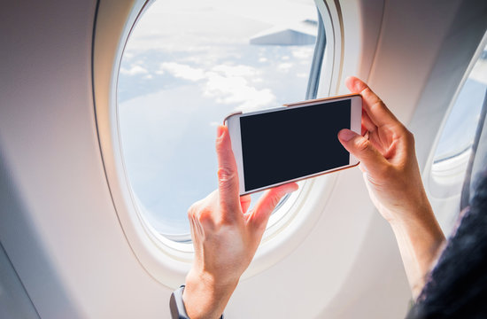 Close up woman hand holding mobile phone and take a photo outside airplane window,Blank screen for adding your design