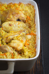 Chicken curry and rice in a ceramic baking dish on a dark background