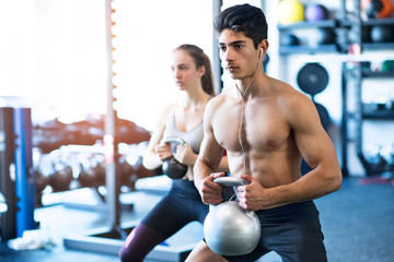 Young fit couple in gym exercising with kettlebell.