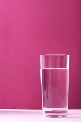 Glass with water on pink background