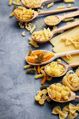 Different kinds of pasta in wooden spoon on grey table