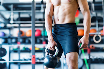 Unrecognizable young fit man in gym exercising with kettlebell.