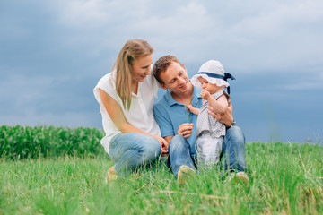 Fototapeta premium Young family in jeans sitting on the grass having fun together. Little girl in panama hat.