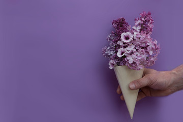 Purple lilac in a cornet held by a hand on lilac background