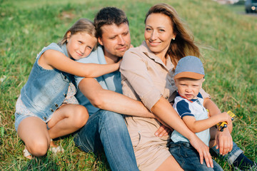 Fototapeta premium Young happy family of four in jeans sitting on the grass. Sunny outdoors. Happy parenting concept