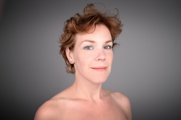 Beautiful red haired aging mature female model against a grey background.