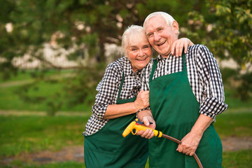 Couple of gardeners, water hose. Senior man and woman smiling. Spring gardening tips.