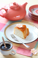 Piece of Tapioca Pudding with Caramel Topping on white plate, cup of coffee and light orange teapot, on colorful napkin.