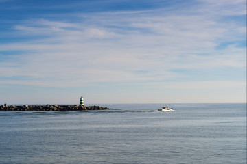 Traditional small fishing boat (traineira) leaving the Portimao harbour with a pier and lighthouse in the background