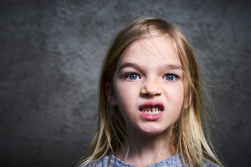 Portrait of child little blond angry girl with gray grunge wall background.