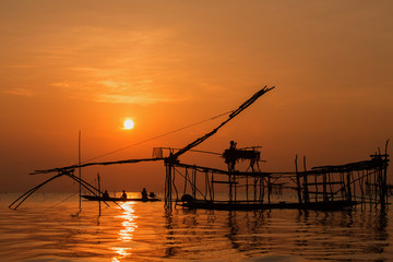Fototapeta na wymiar Asian fisherman on wooden boat casting a net for catching freshwater fish in nature river in the early morning with sunrise