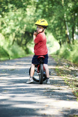 Naklejka premium Young boy riding bicycle on a summer day at asphalt road. Bicycle path