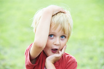 Naklejka premium Portrait of a funny little boy making faces outdoors with green grass lawn background