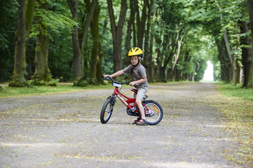 Naklejka premium Child boy on a bicycle in the forest in summer. Boy cycling outdoors in safety helmet. Sun flare effect added
