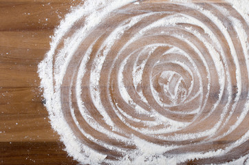 White flour with trace of fingers on a wooden cutting board. Top view, close up.