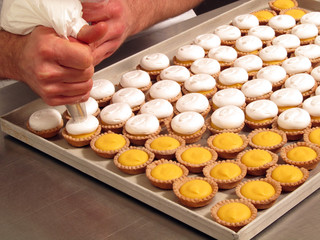 Pastelero preparando pasteles con crema en una cocina industrial.