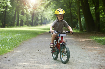 Fototapeta premium Child boy on a bicycle in the forest in summer. Boy cycling outdoors in safety helmet. 