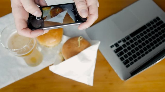 Person with smartphone phone photographing burger with laptop. Fast food dish. Top view