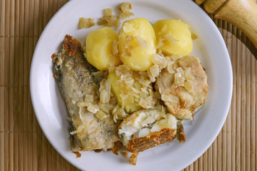 Fried fish and boiled potatoes lies on a plate on a bamboo napkin. Close-up, selective focus.