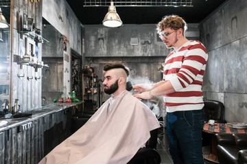 Hairdresser man shaves a client with a beard in a barbershop